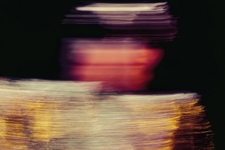 Motion-blurred photo of Karen O from the Yeah Yeah Yeahs performing on stage in a shimmering gold outfit against a dark background.